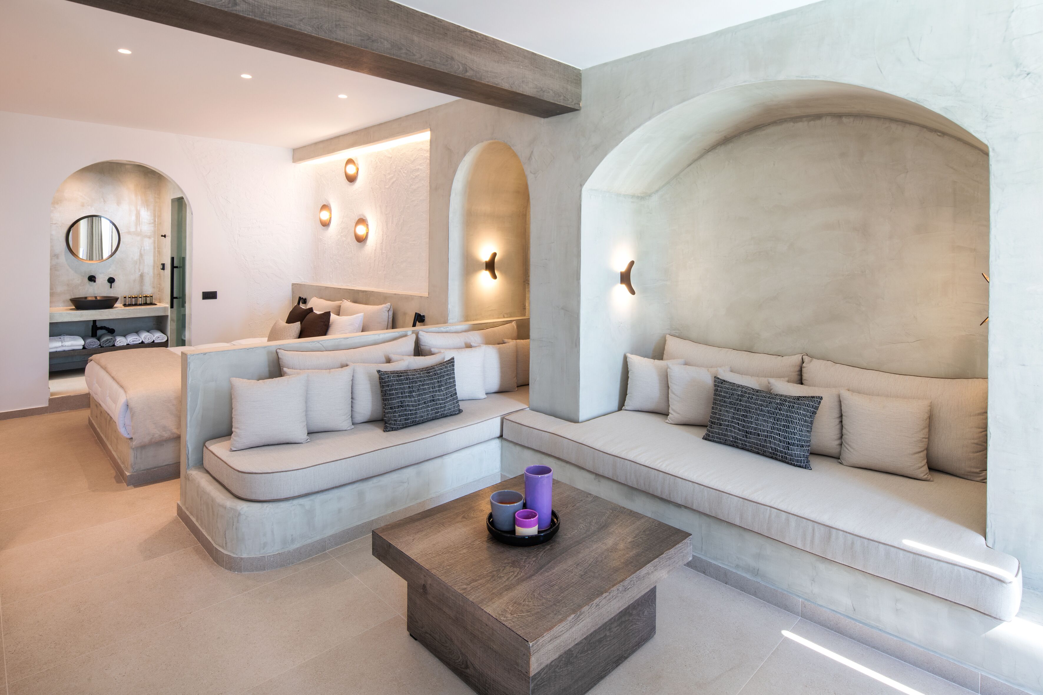 A modern living room with a built-in sofa, a coffee table, and a built-in kitchen area with a sink and shelves.