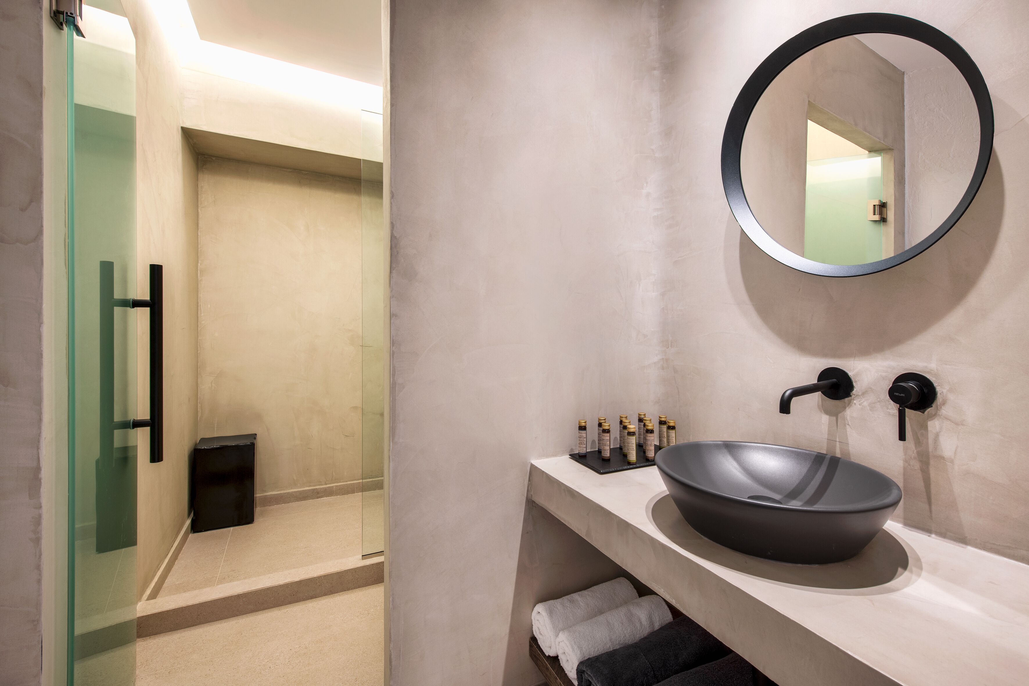 Une salle de bain moderne avec une douche à parois de verre, un miroir rond et un lavabo sur colonne.