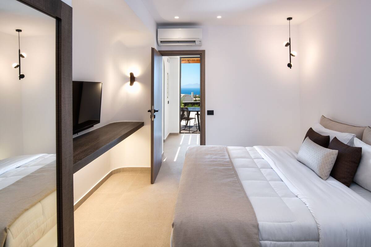 Un dormitorio moderno con cama, televisor y balcón con vistas.