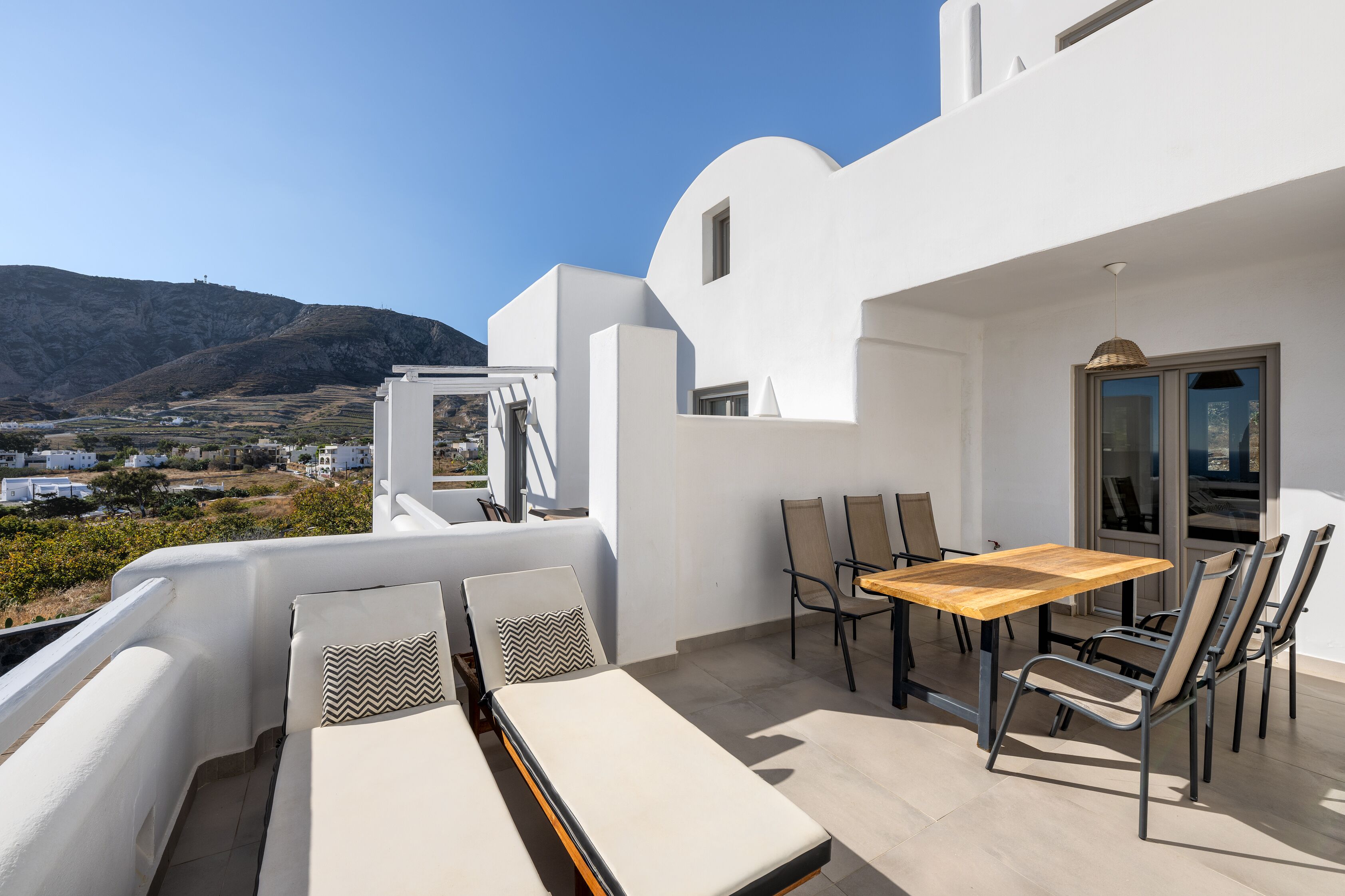 A balcony with a table and chairs, a sofa, and a view of the landscape.