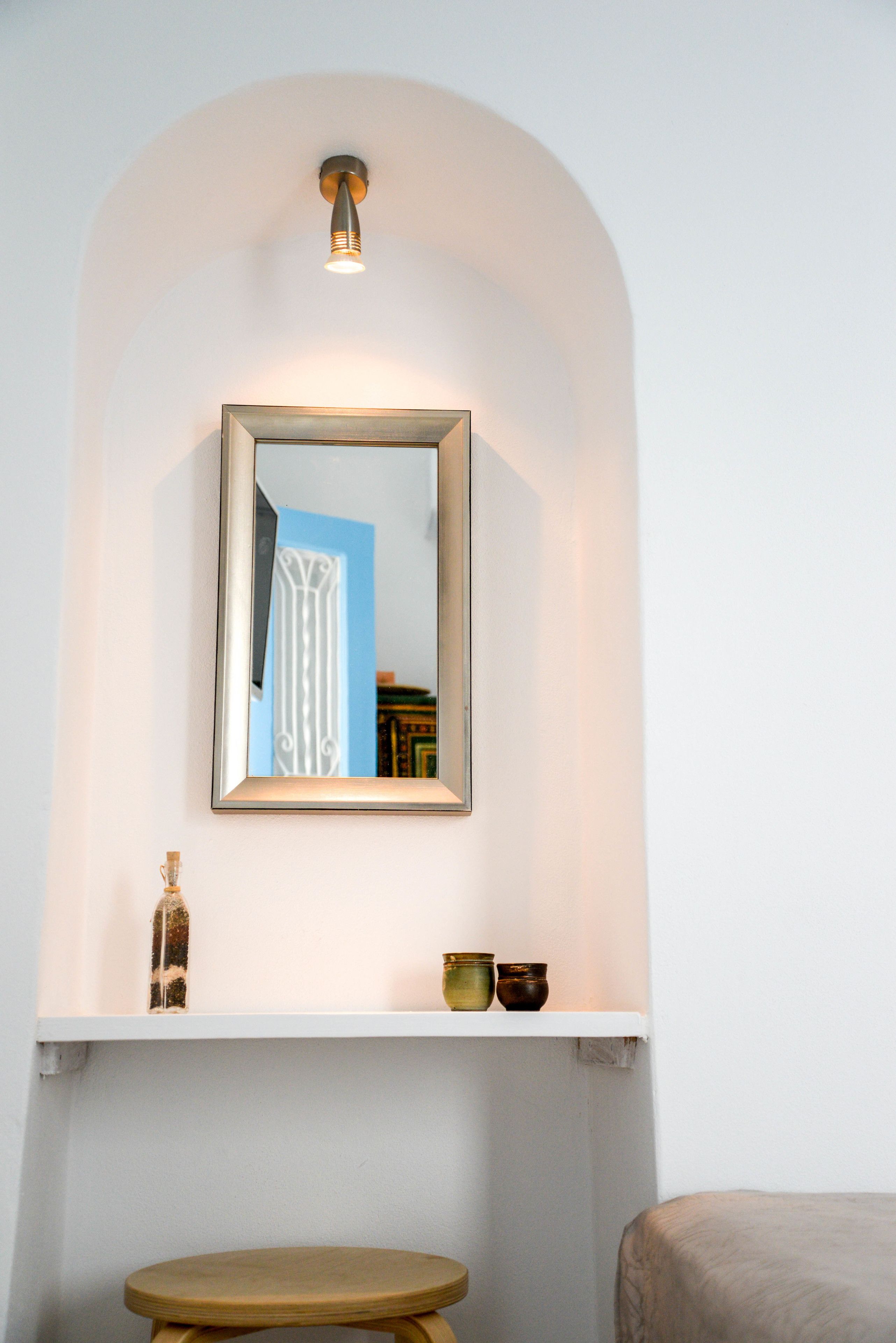 Een badkamer met een spiegel, een plank met decoratieve objecten en een houten kruk.