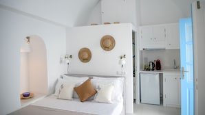 A bedroom with a bed, bedside table, and a small kitchenette with a refrigerator and sink. - Genesis Cave Houses (Santorini)