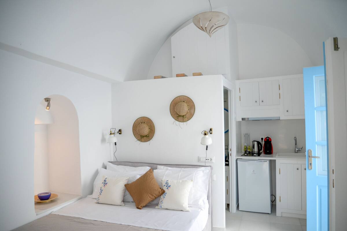 A bedroom with a bed, bedside table, and a small kitchenette with a refrigerator and sink.
