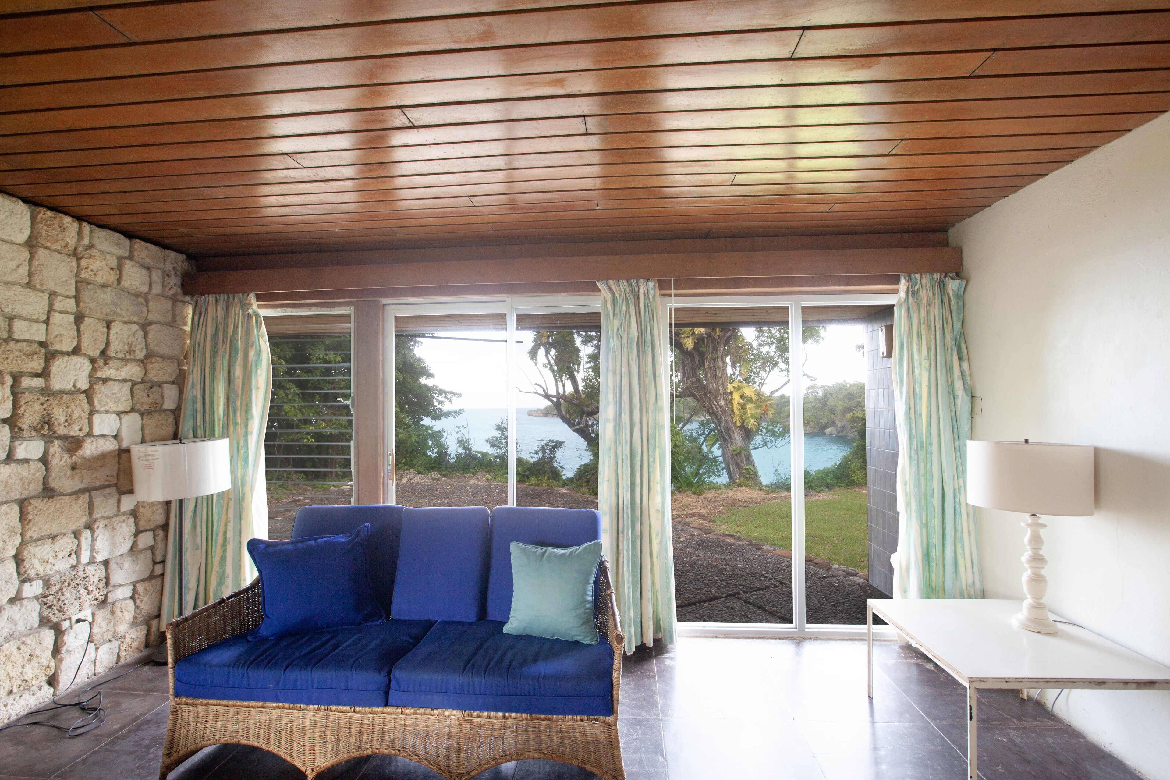 A room with a wicker sofa, a small table, and a stone wall.