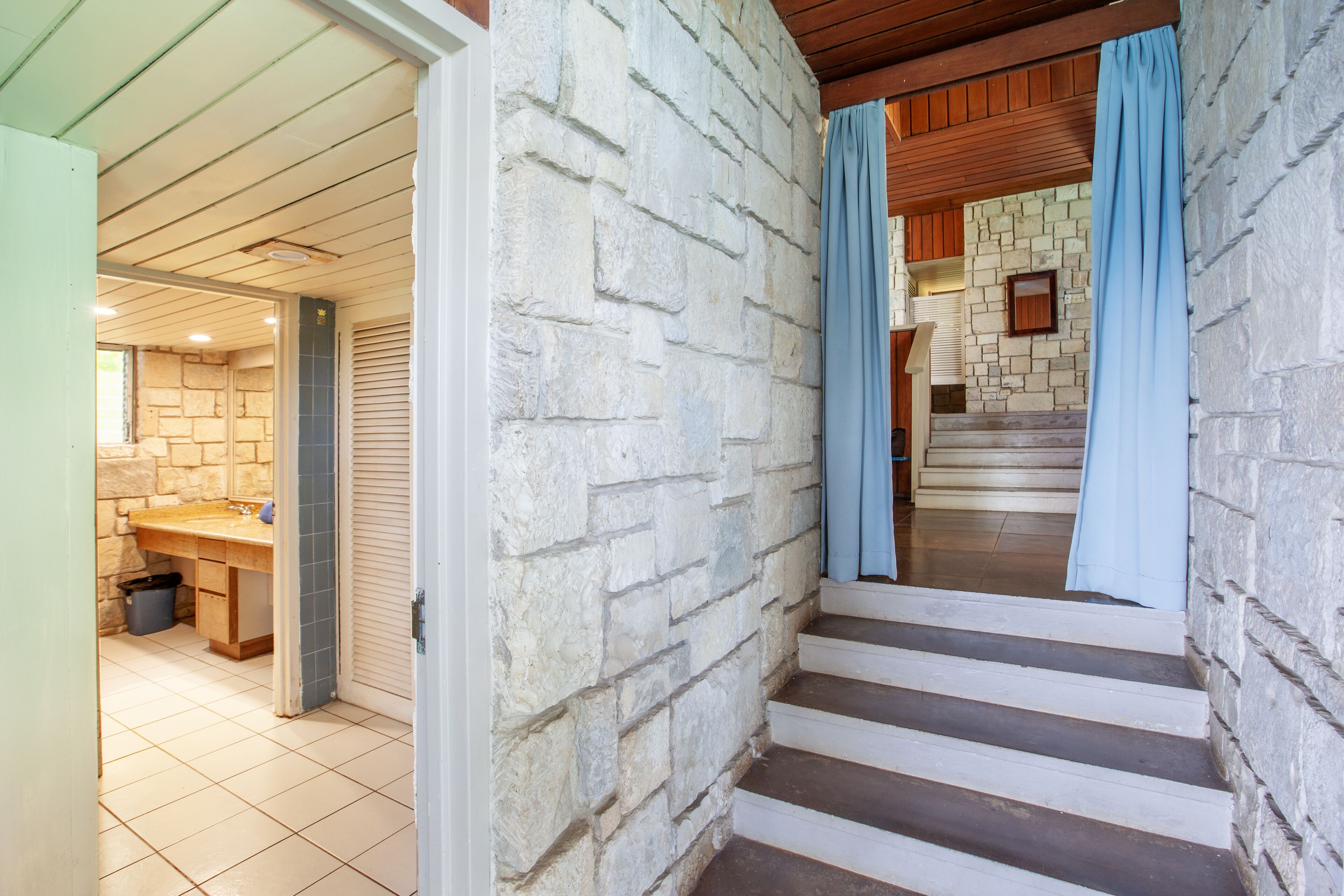 A staircase with stone walls and blue curtains, leading to a room with a wooden ceiling and a tiled floor.