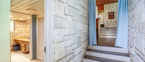 A staircase with stone walls and blue curtains, leading to a room with a wooden ceiling and a tiled floor.