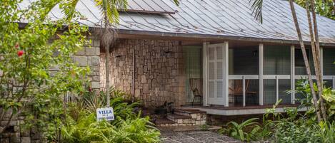 A stone house with a metal roof, a porch with a chair, and a sign reading "Villa."