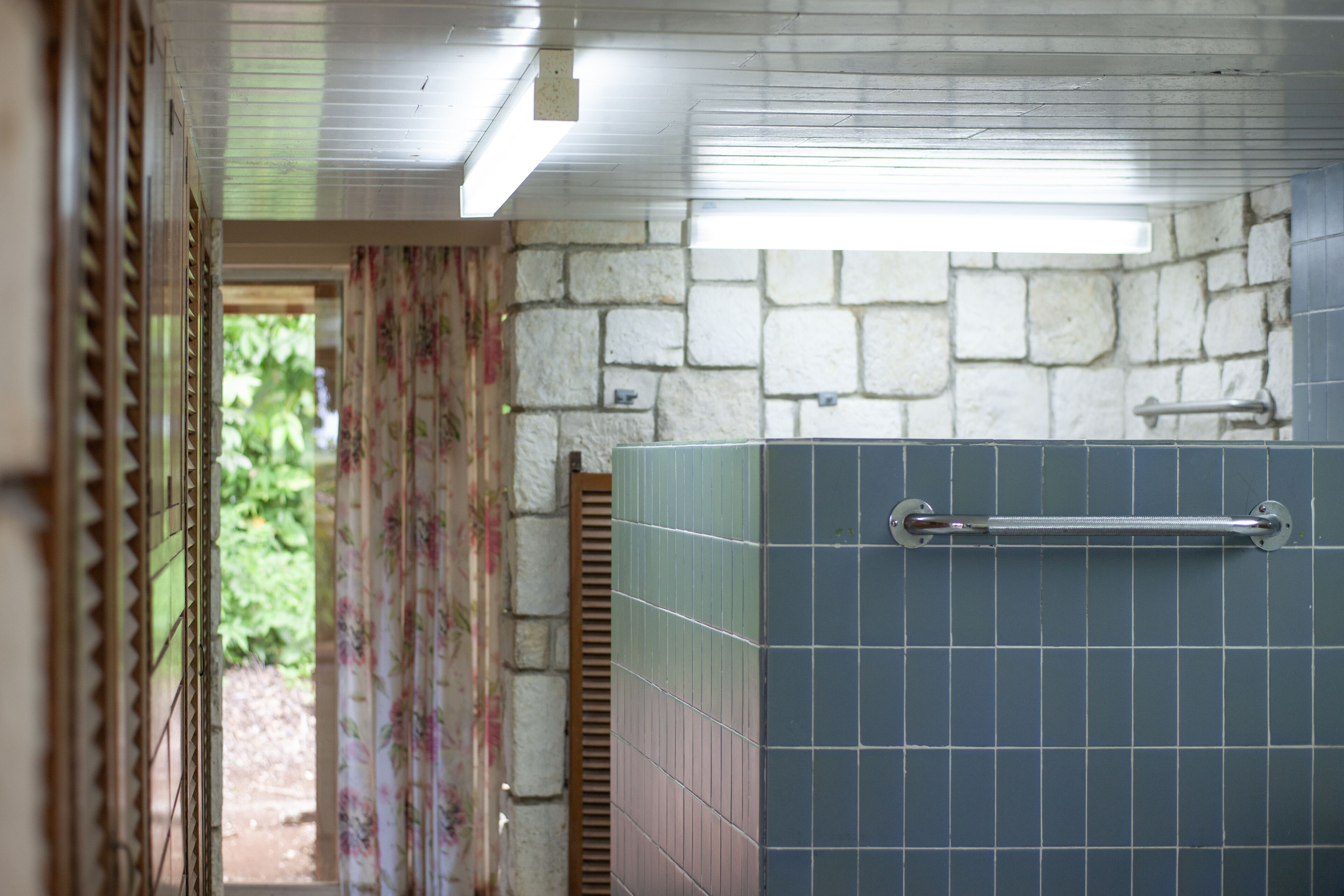 Un baño con pared de piedra, zona de ducha con azulejos y puerta que da a un área exterior.