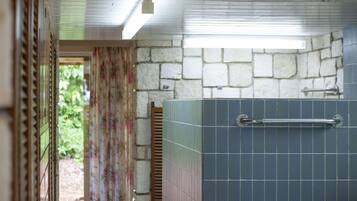 Un baño con pared de piedra, zona de ducha con azulejos y puerta que da a un área exterior.