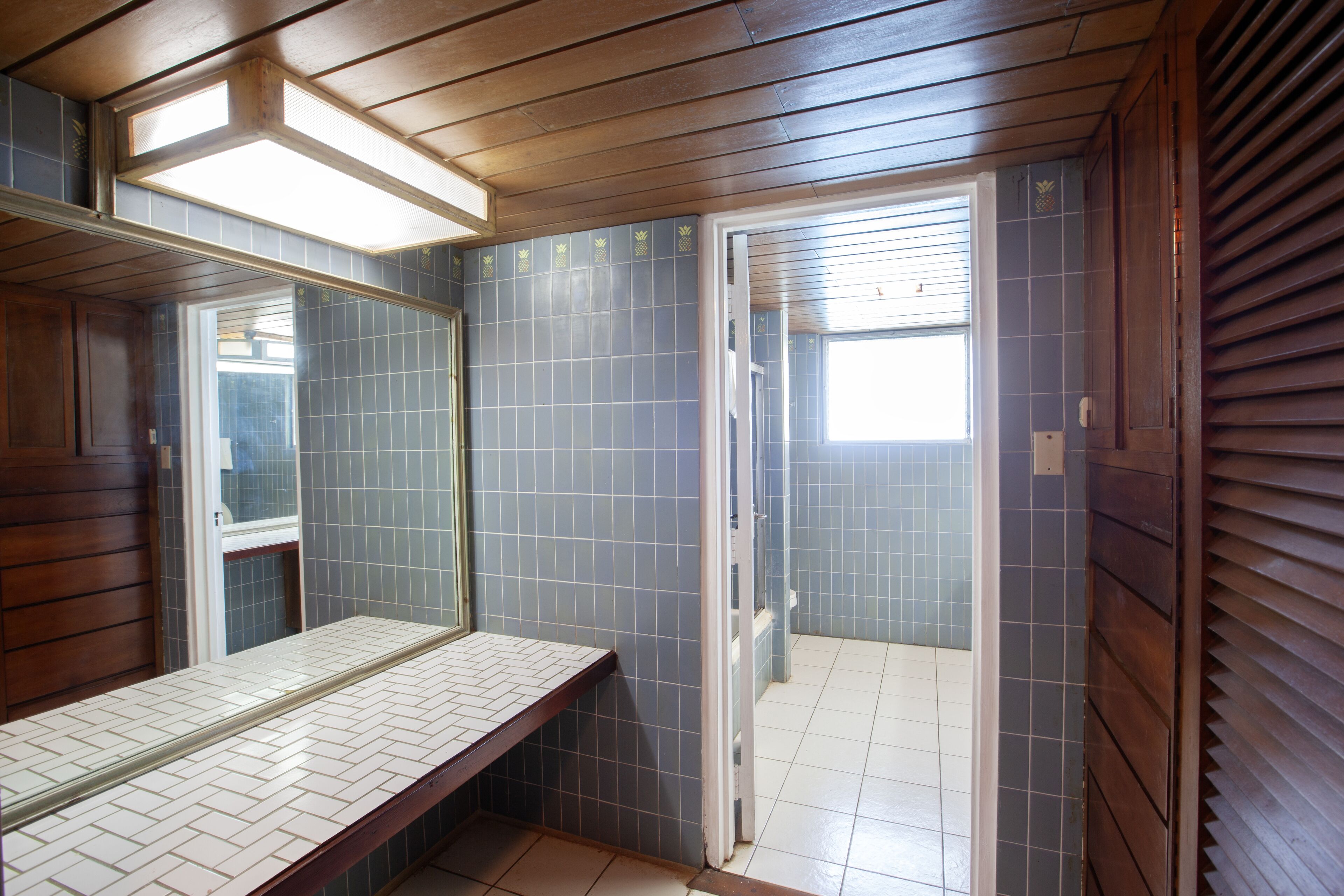Un baño con techo de madera, zona de ducha con azulejos y un espejo sobre el lavabo.