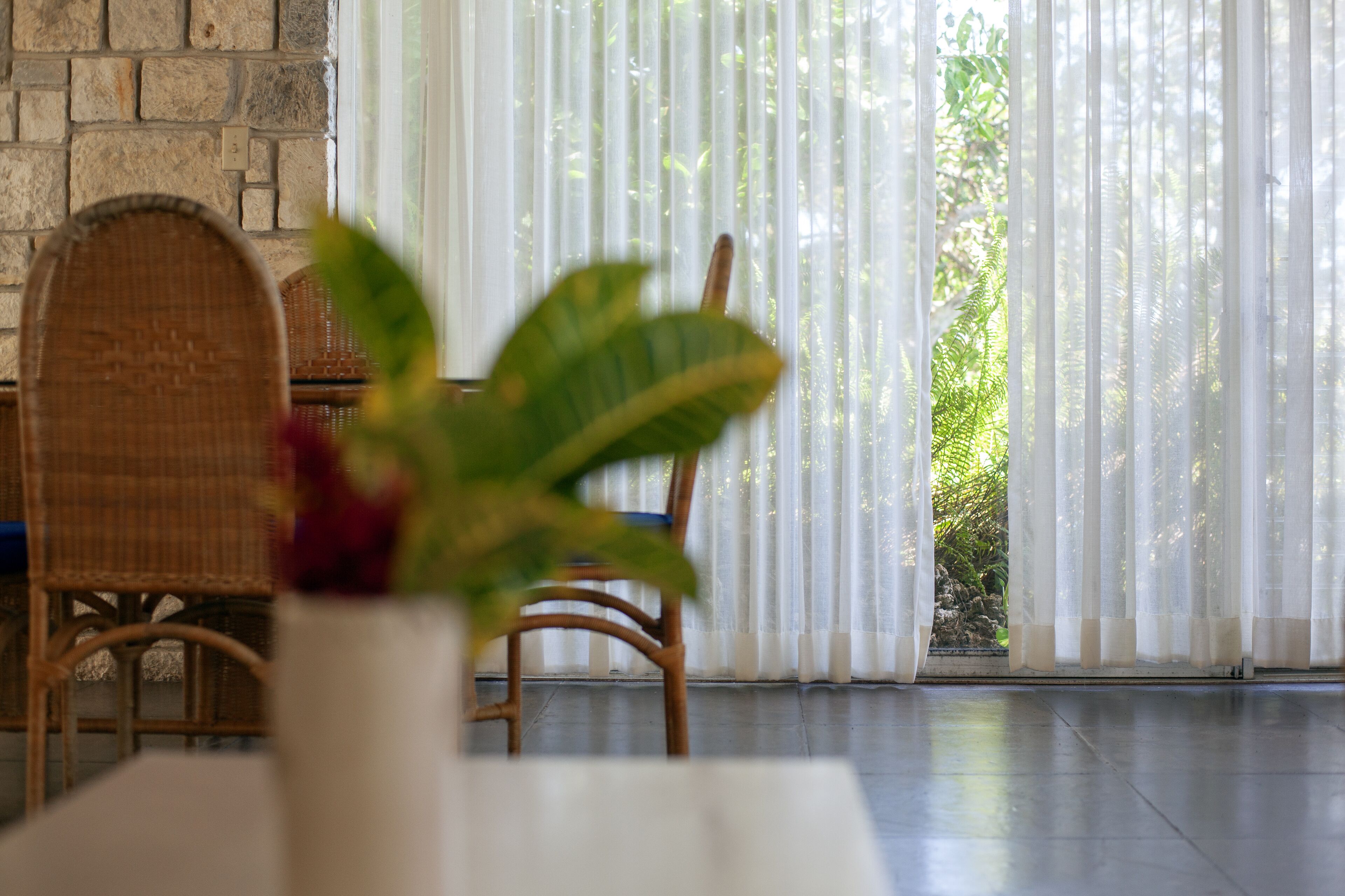 Una habitación con pared de piedra, una silla de mimbre, una mesa blanca y una planta en un florero blanco.