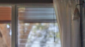 A bed with a view of a blue body of water through a window with blinds.