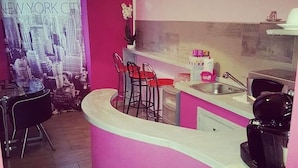 Una cocina con pared de acento rosa, una barra con taburetes rojos y un cartel con un paisaje urbano.