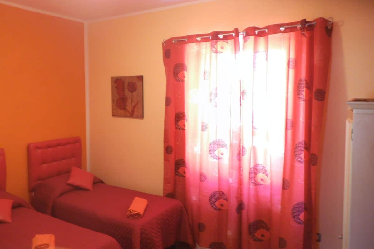 A room with two beds, a red headboard, a painting on the wall, and a curtain with a pattern.