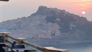 Un paisaje costero con una colina destacada o una pequeña isla, mar en calma y un sol poniéndose.