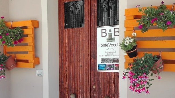 Una puerta de madera con un letrero, un balcón con barandas metálicas y plantas en macetas.