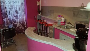 Una cocina con pared rosa, una zona de bar con taburetes, una cafetera y un cartel de la ciudad de Nueva York.