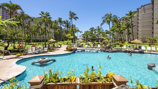 A large outdoor swimming pool with a rock feature, surrounded by palm trees and lounge chairs. - Kaanapali Shores Studio 742 Studio Bedroom Condo by RedAwning (Lahaina)
