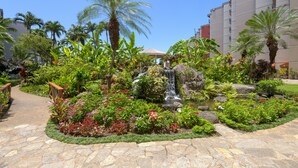 A landscaped garden with a waterfall, palm trees, and a stone pathway. - Kaanapali Shores Studio 742 Studio Bedroom Condo by RedAwning (Lahaina)