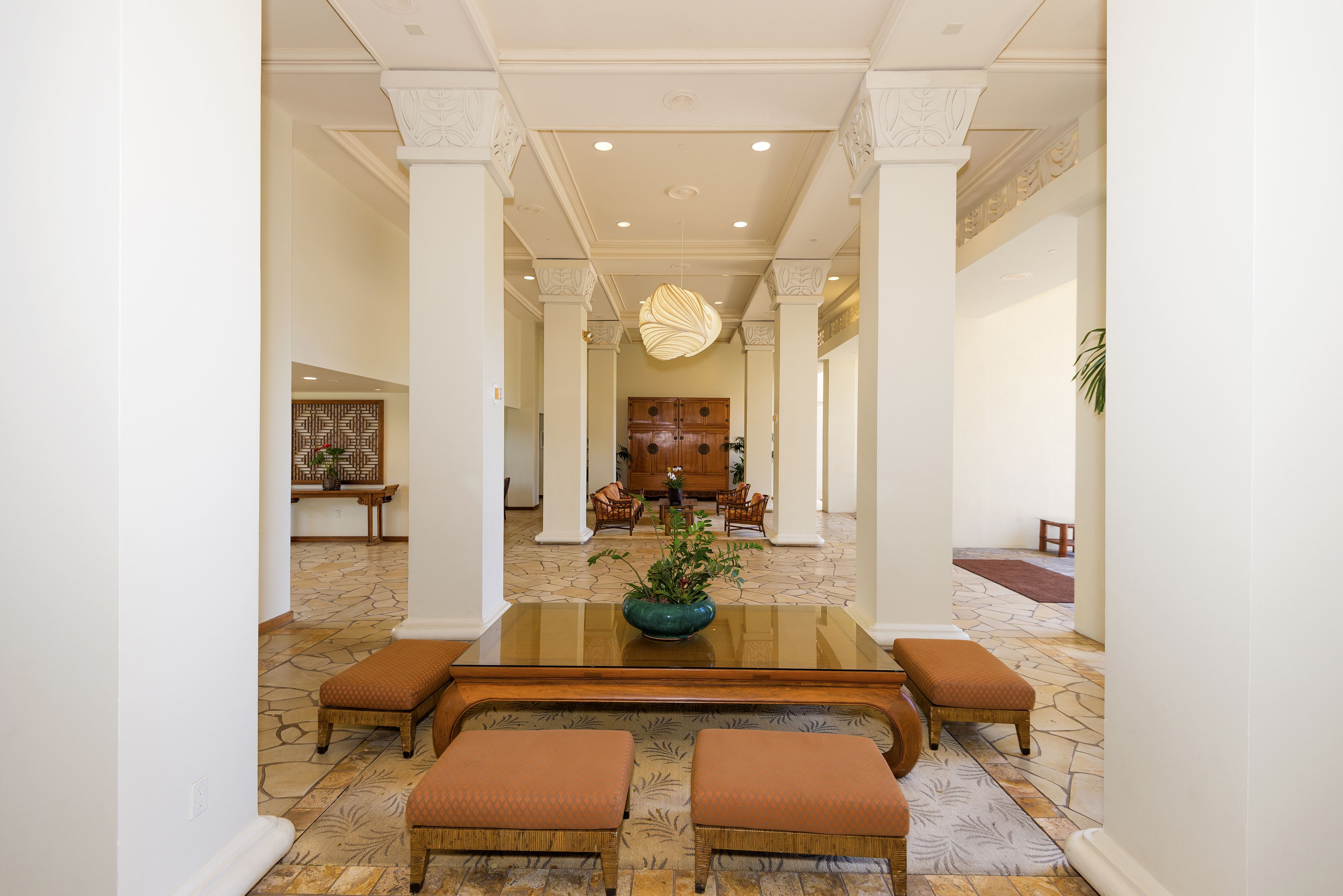 Um hall espaçoso com uma mesa central de vidro, duas opções de assento acolchoadas e uma planta decorativa.