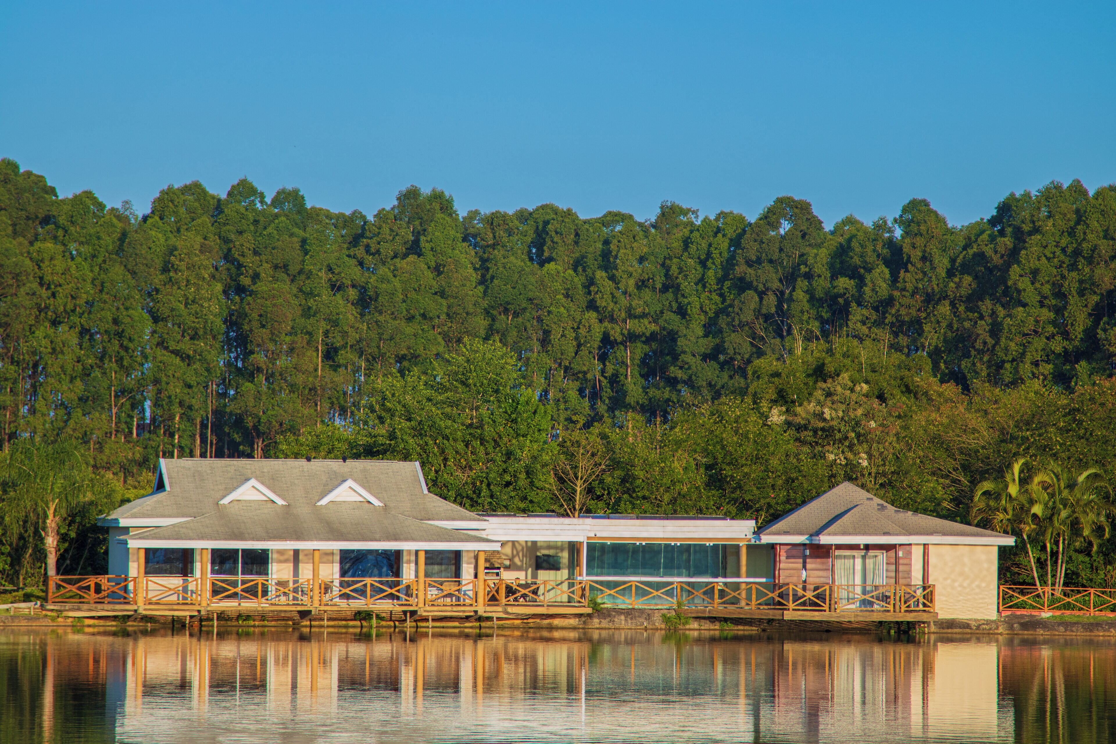 Uma cabana à beira do lago com varanda, janelas amplas e reflexo na água.