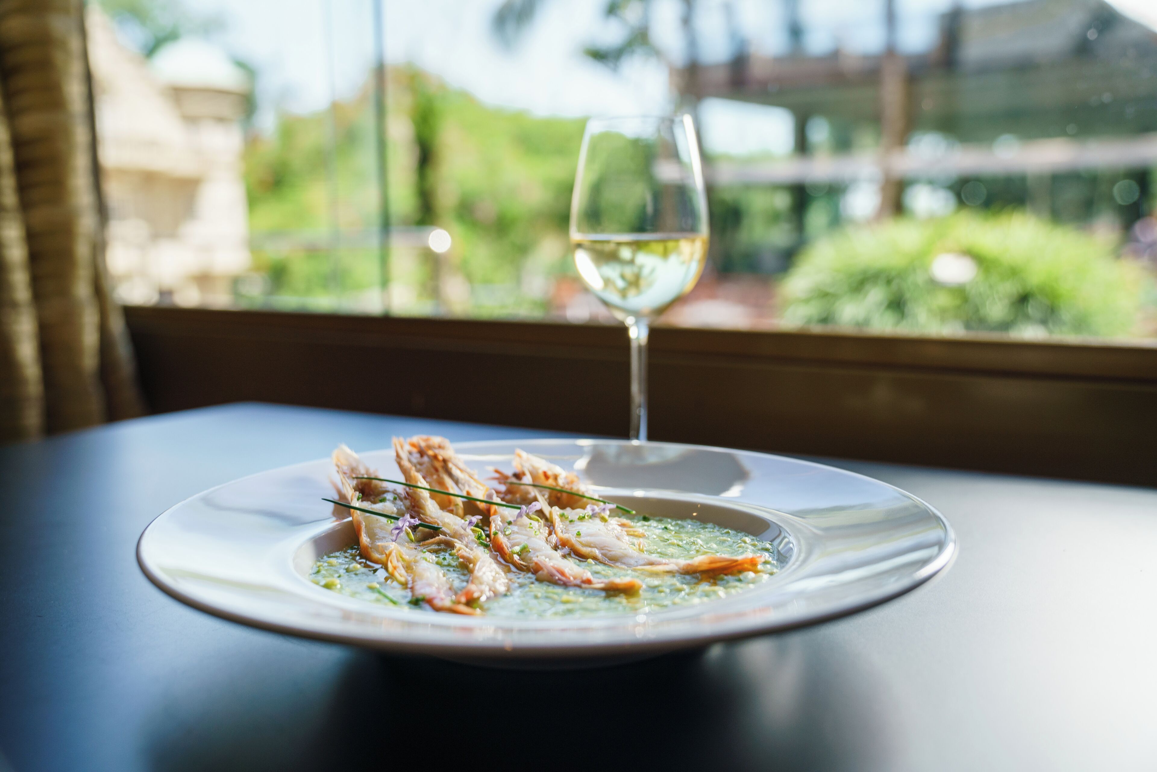 Prato de frutos do mar com um copo de vinho branco sobre uma mesa junto a uma janela.