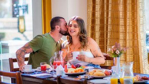 Un couple est assis à une table où est servi le petit-déjeuner, et sur laquelle on peut voir une variété d'aliments et de boissons.