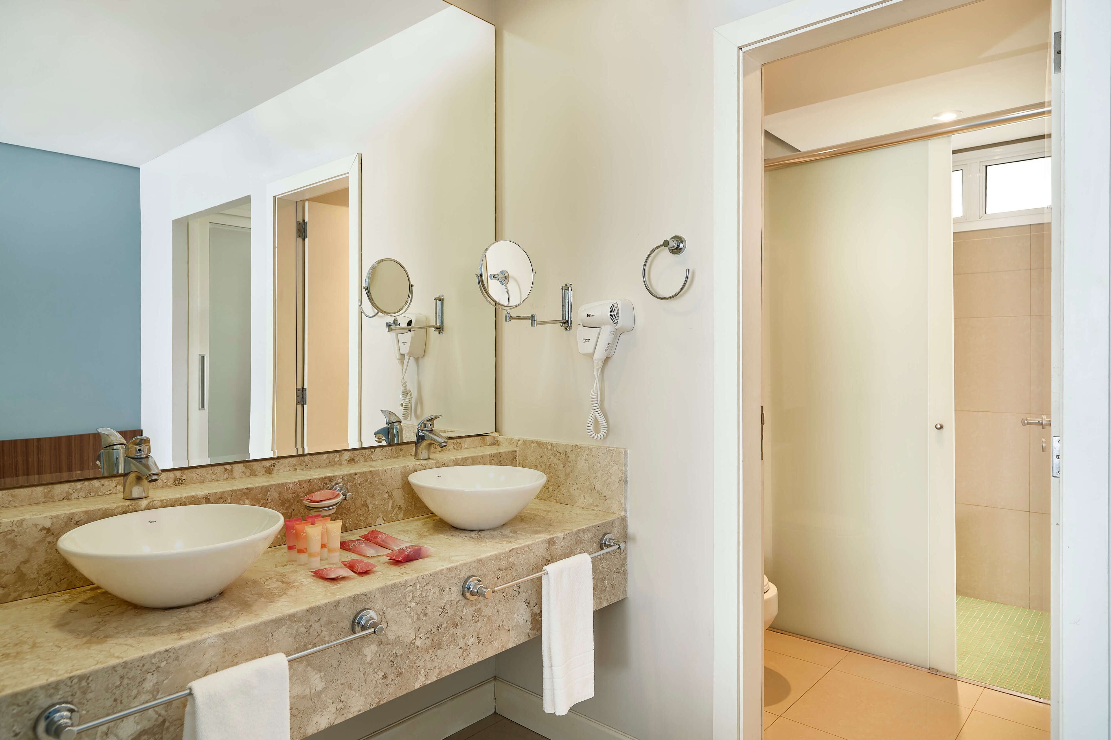 A bathroom with two sinks, a large mirror, a hairdryer, and a toilet.