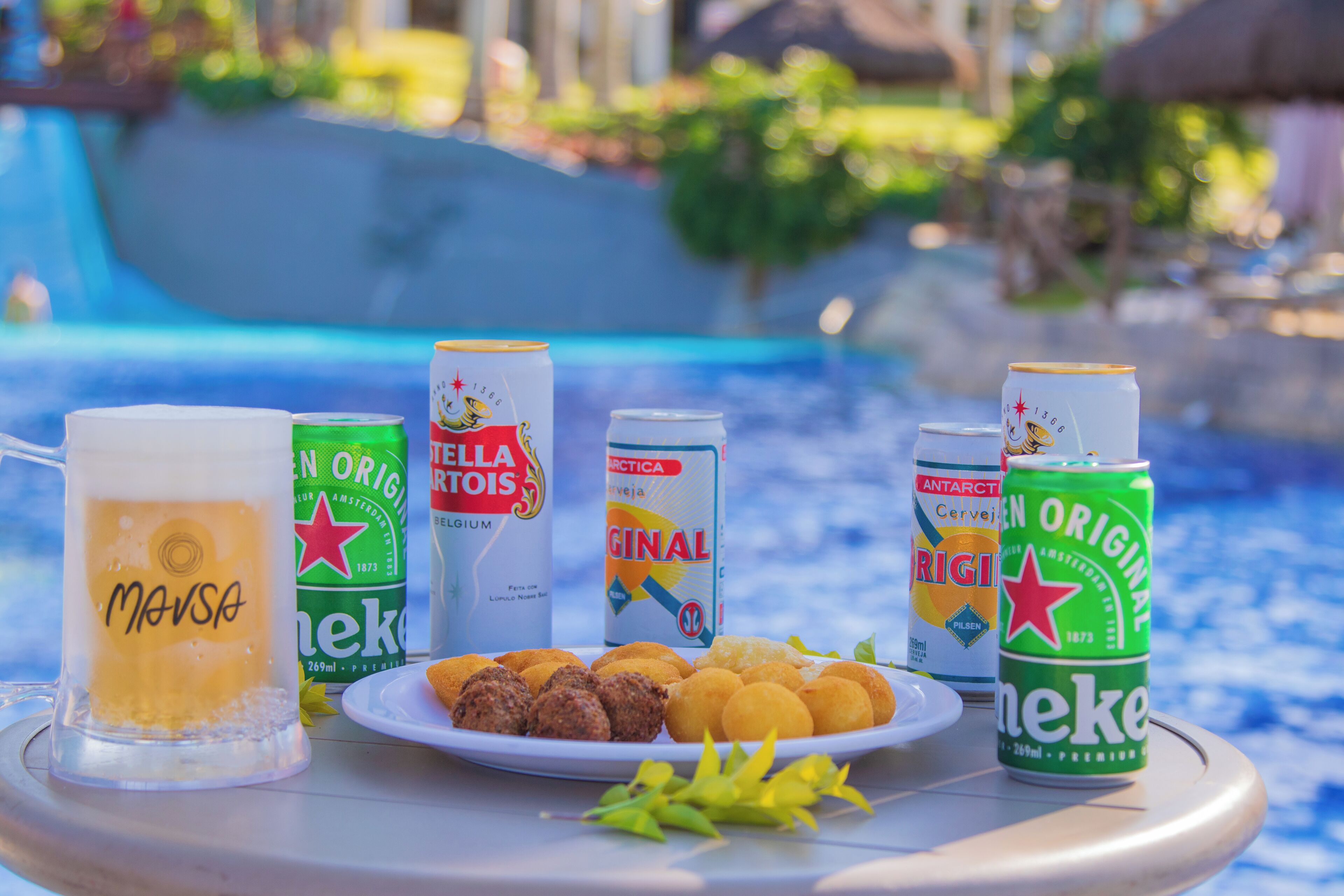 A table with a glass of beer, several cans of beer, and a plate of food.