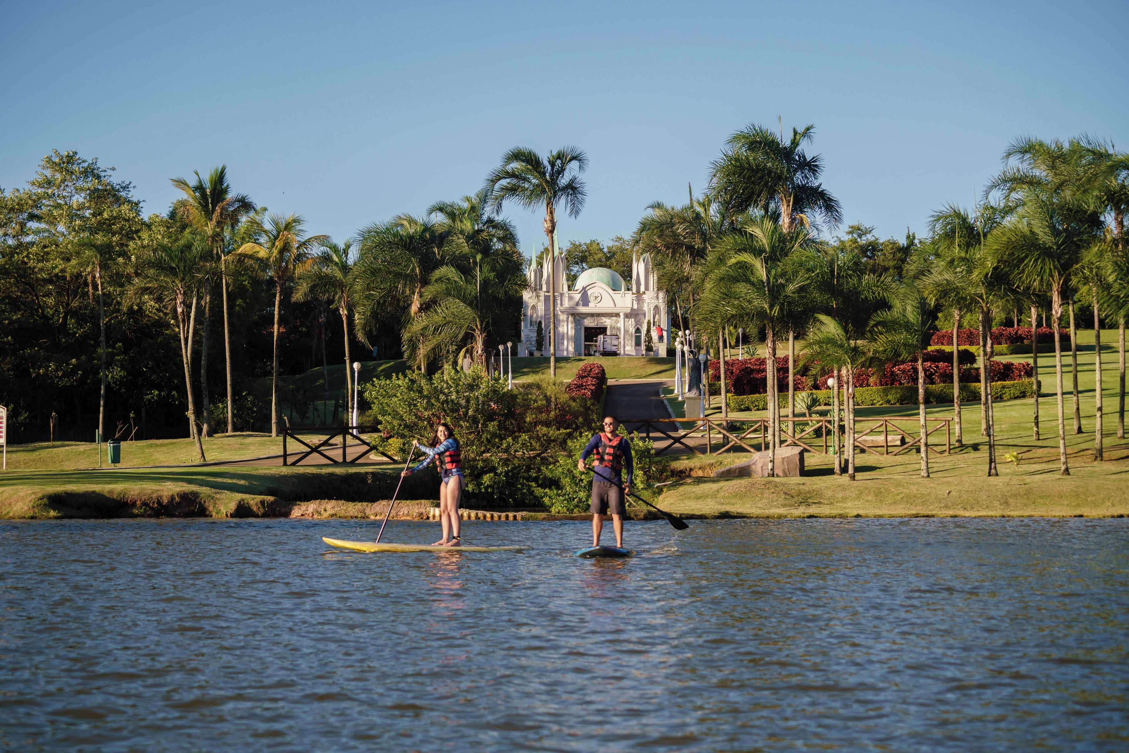 Two people paddleboarding on a calm lake with a tropical resort in the background.