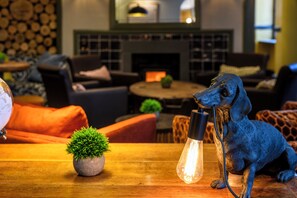 A room with a sofa, a small table with a plant, and a decorative dog statue holding a light bulb. - The Crown Hotel (Lynton)