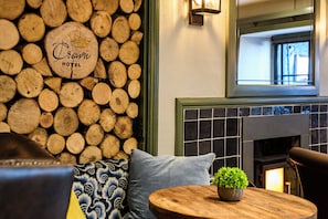 A log wall with a sign reading 'Crystal Hotel,' a fireplace, a round wooden table with a plant, and a sofa with patterned cushions. - The Crown Hotel (Lynton)