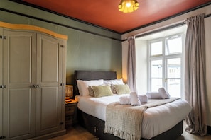 A bedroom with a bed, bedside table, wardrobe, and a window with curtains. - The Crown Hotel (Lynton)
