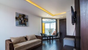 Una sala de estar moderna con un sofá, una mesa de comedor con sillas, un televisor montado en la pared y un ventanal con vistas al exterior.