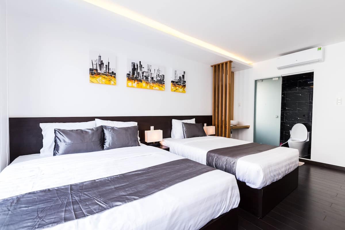 Ett hotellrum med två sängar, ett konstverk med en stadsbild på väggen, en träpanel, en spegel och en luftkonditioneringsanläggning.