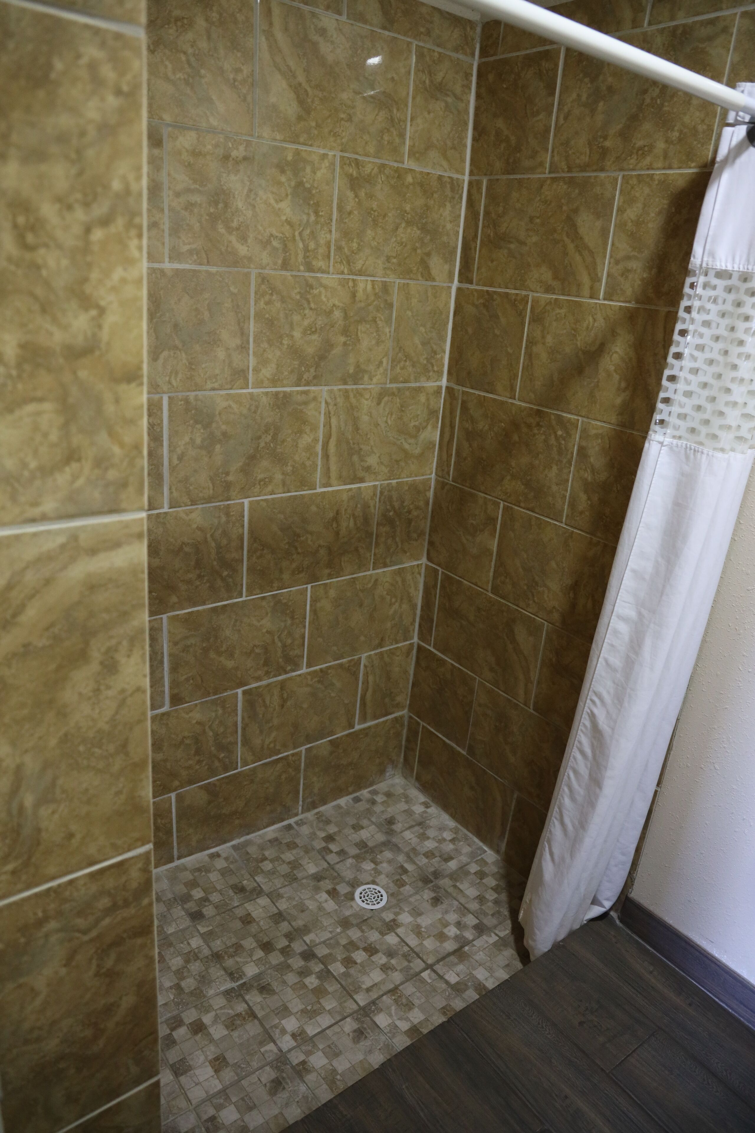 A shower area with tiled walls and floor, a shower curtain, and a drain.