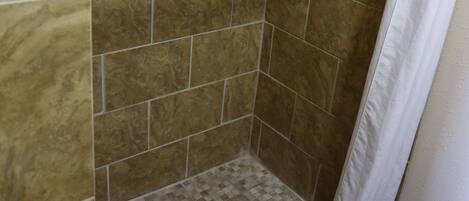 A shower area with tiled walls and floor, a shower curtain, and a drain.