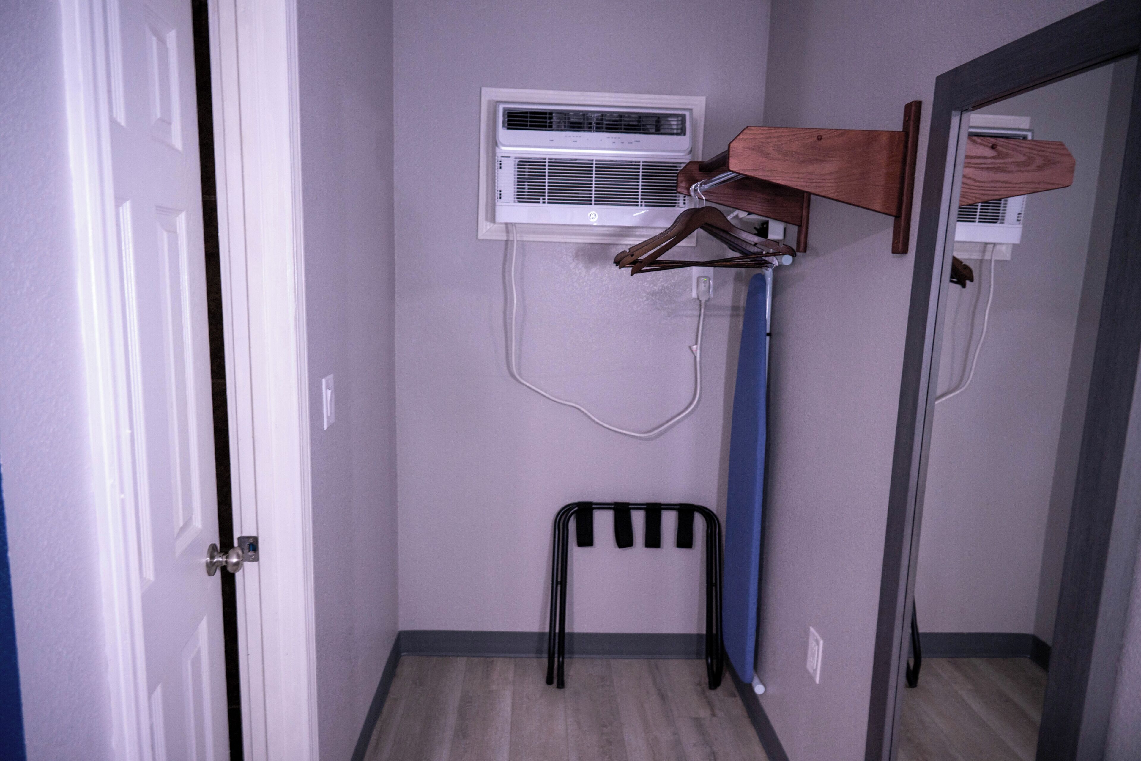 A room with a door, an air conditioning unit, a wooden hanger, and a black chair.