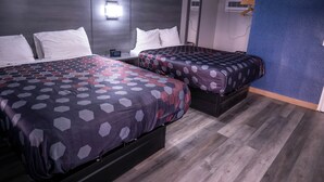 A hotel room with two beds, each with a patterned bedspread, a nightstand with a digital clock, and a wall-mounted air conditioner. - Budget Inn (Alamogordo)