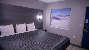 Hotelkamer met een groot bed, nachtkastje, wandlamp en raam met uitzicht op een woestijn.