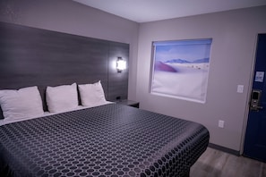 Une chambre d’hôtel avec un grand lit, une table de chevet, une lampe fixée au mur et une fenêtre donnant sur le désert.