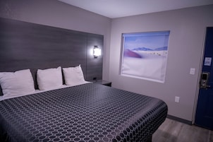 A hotel room with a large bed, a nightstand, a wall-mounted light, and a window with a desert view.