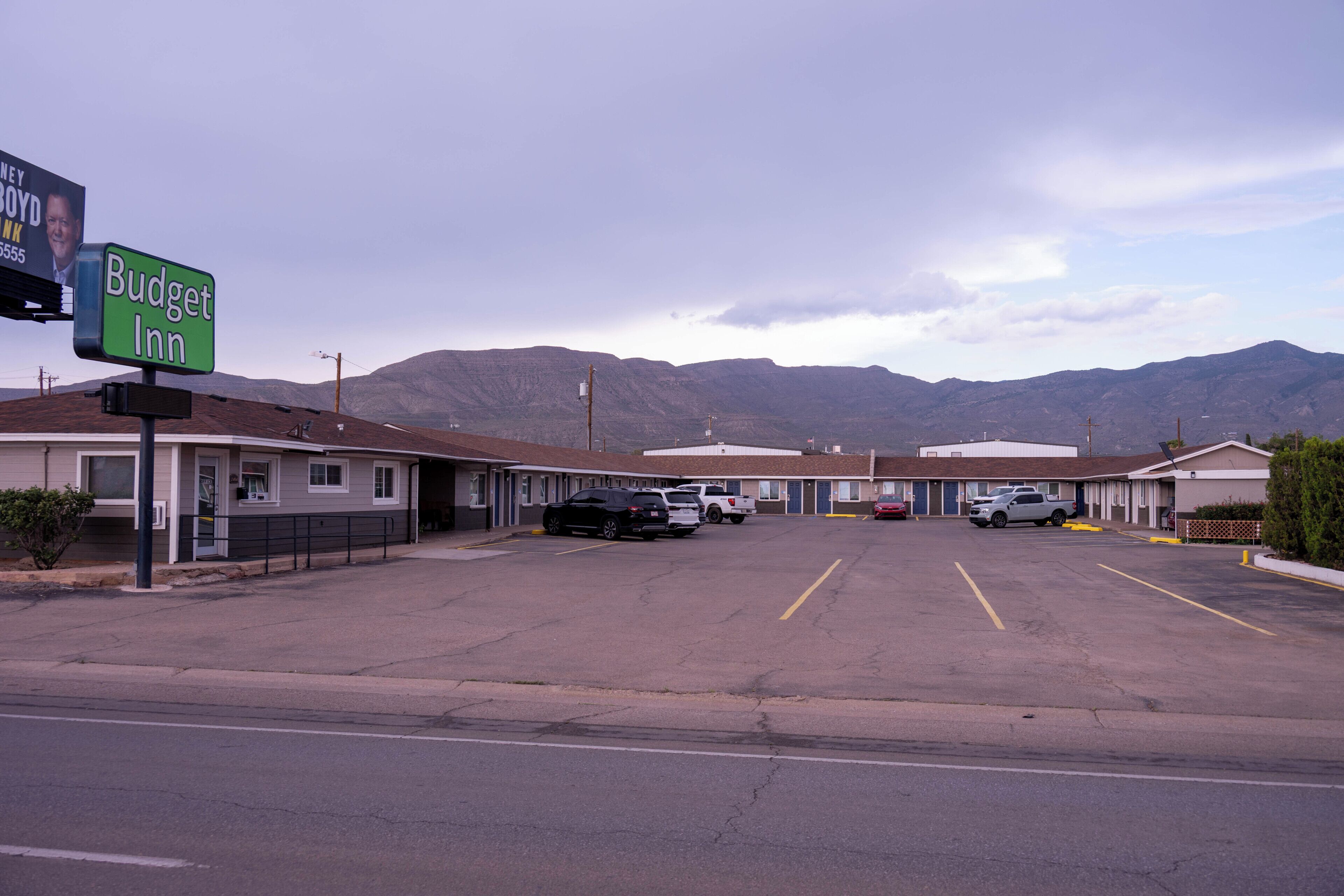 A Budget Inn with a parking lot, a mountain backdrop, and a clear sky.