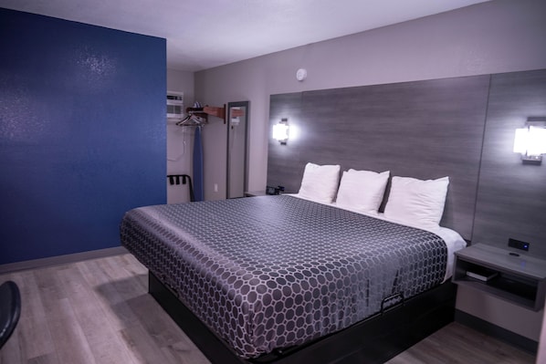 Una habitación de hotel con una cama, una mesita de noche, un espejo y una lámpara de pared.