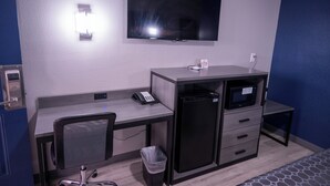 A hotel room with a flat-screen TV mounted on the wall, a desk with a telephone, a microwave, and a trash bin. - Budget Inn (Alamogordo)