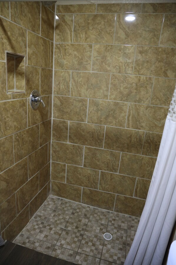 A shower area with tiled walls and floor, a showerhead, and a curtain.