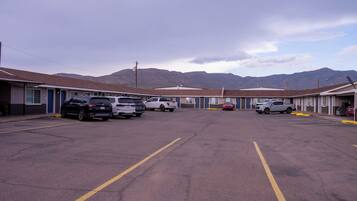 A parking lot with several vehicles, including SUVs and a pickup truck, in front of a row of motel buildings with a mountainous backdrop.