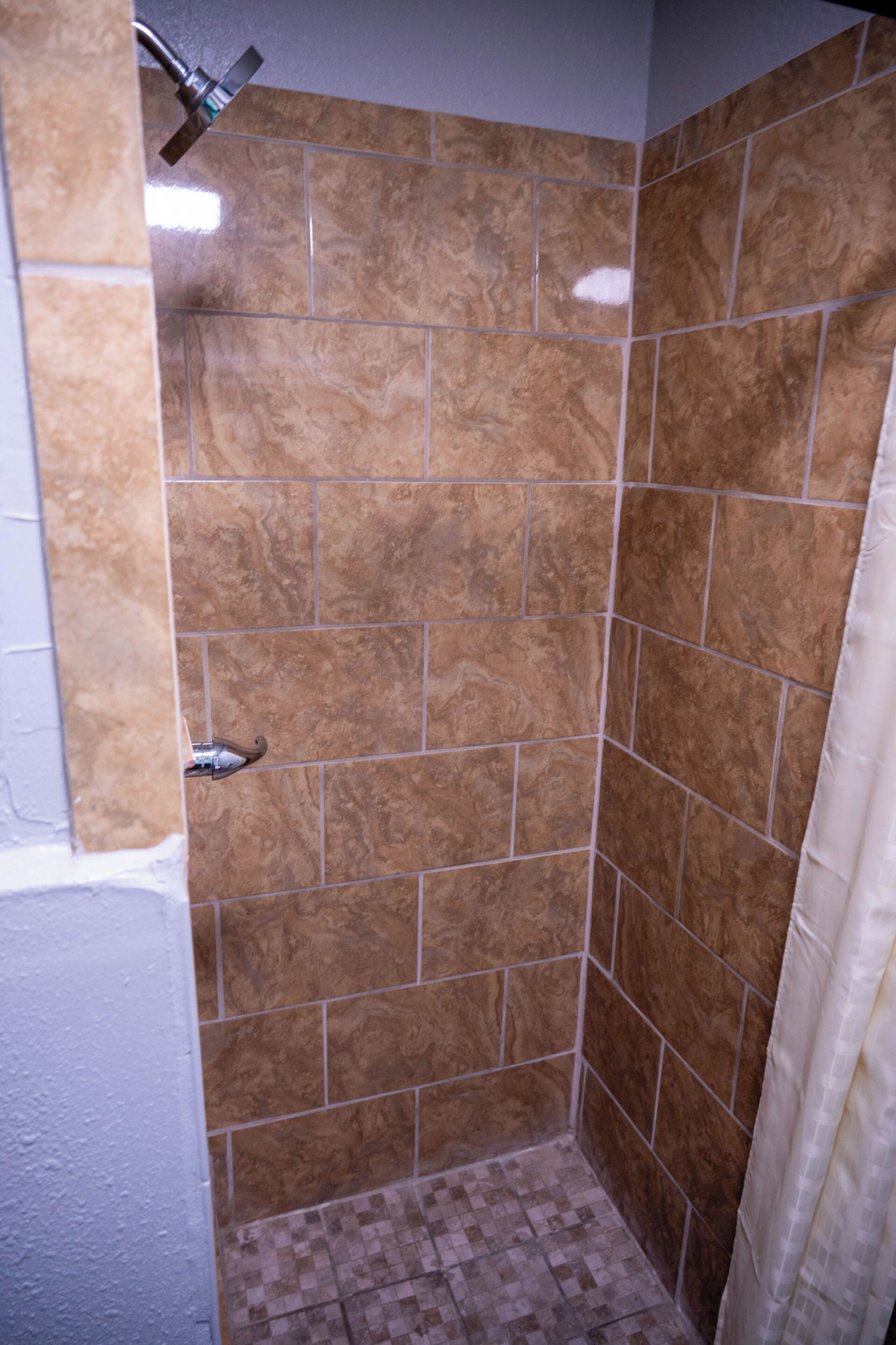A shower area with brown tiles, a showerhead, and a curtain.