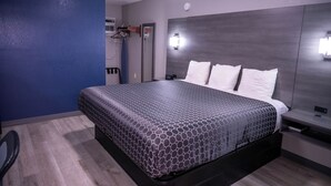 A modern hotel room with a large bed, a wardrobe, a desk, and a mirror.