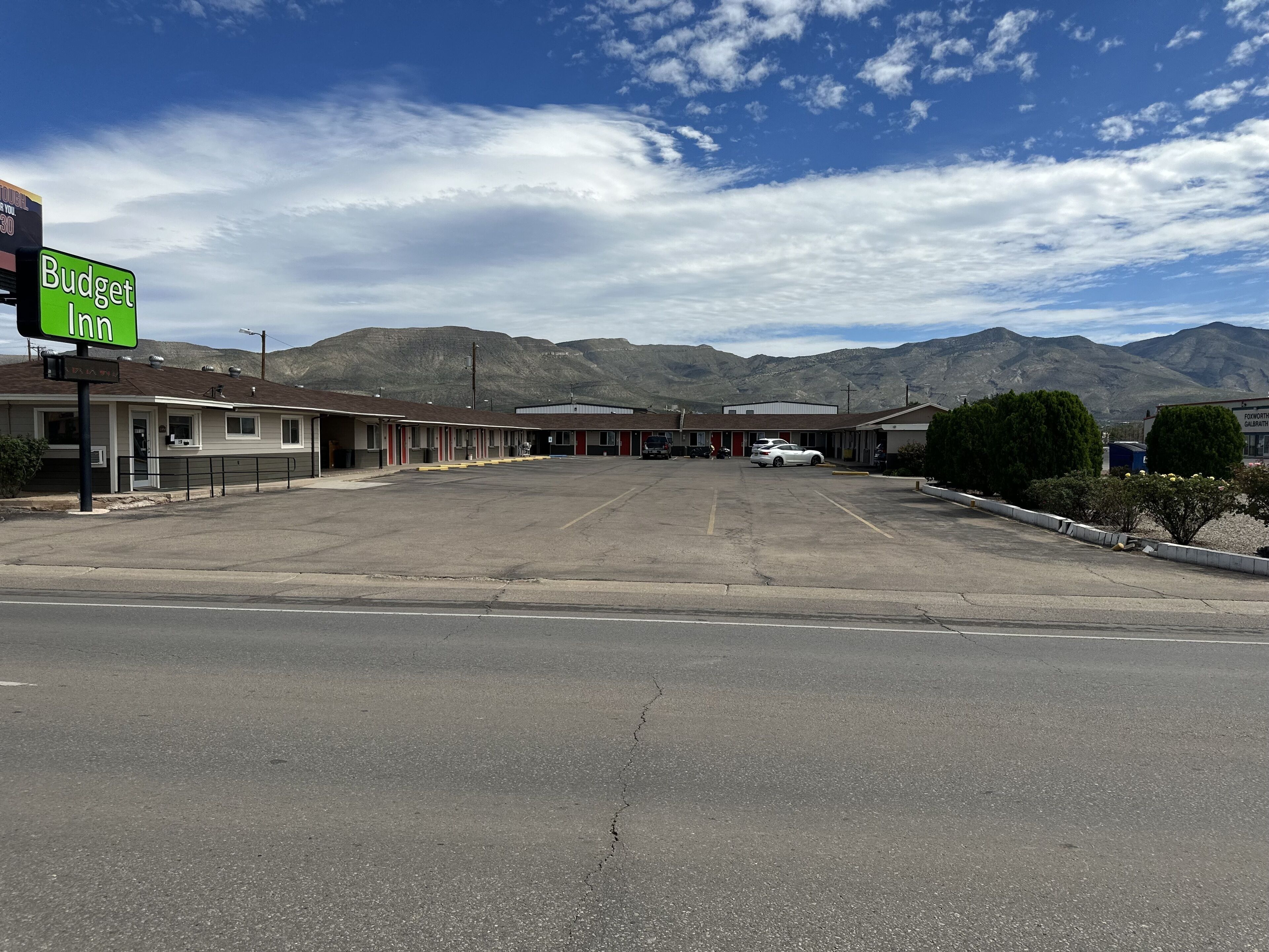 A motel with a large parking lot, multiple motel units, and mountains in the background.